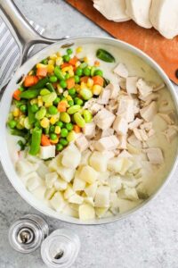 menambahkan kentang, ayam, dan sayuran ke dalam campuran mentega dan bawang bombay untuk membuat Chicken Pot Pie Casserole