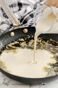 menuangkan krim ke dalam campuran mentega untuk membuat Homemade Chicken Alfredo
