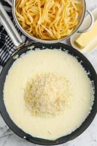 menambahkan parmesan ke saus untuk membuat Alfredo Ayam Buatan Sendiri