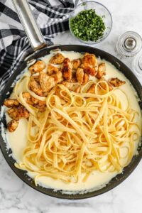 menambahkan ayam dan mie ke dalam saus untuk membuat Alfredo Ayam Buatan Sendiri