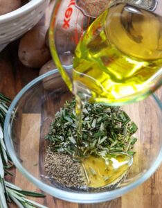 Bahan-bahan untuk Rosemary menghancurkan kentang dalam mangkuk kaca yang telah dituang minyak