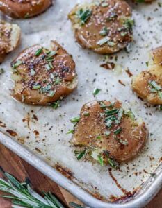 Rosemary menghancurkan kentang di atas loyang dengan rosemary di sampingnya