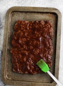 mengoleskan saus bbq pada daging giling yang dimasak untuk membuat Slider